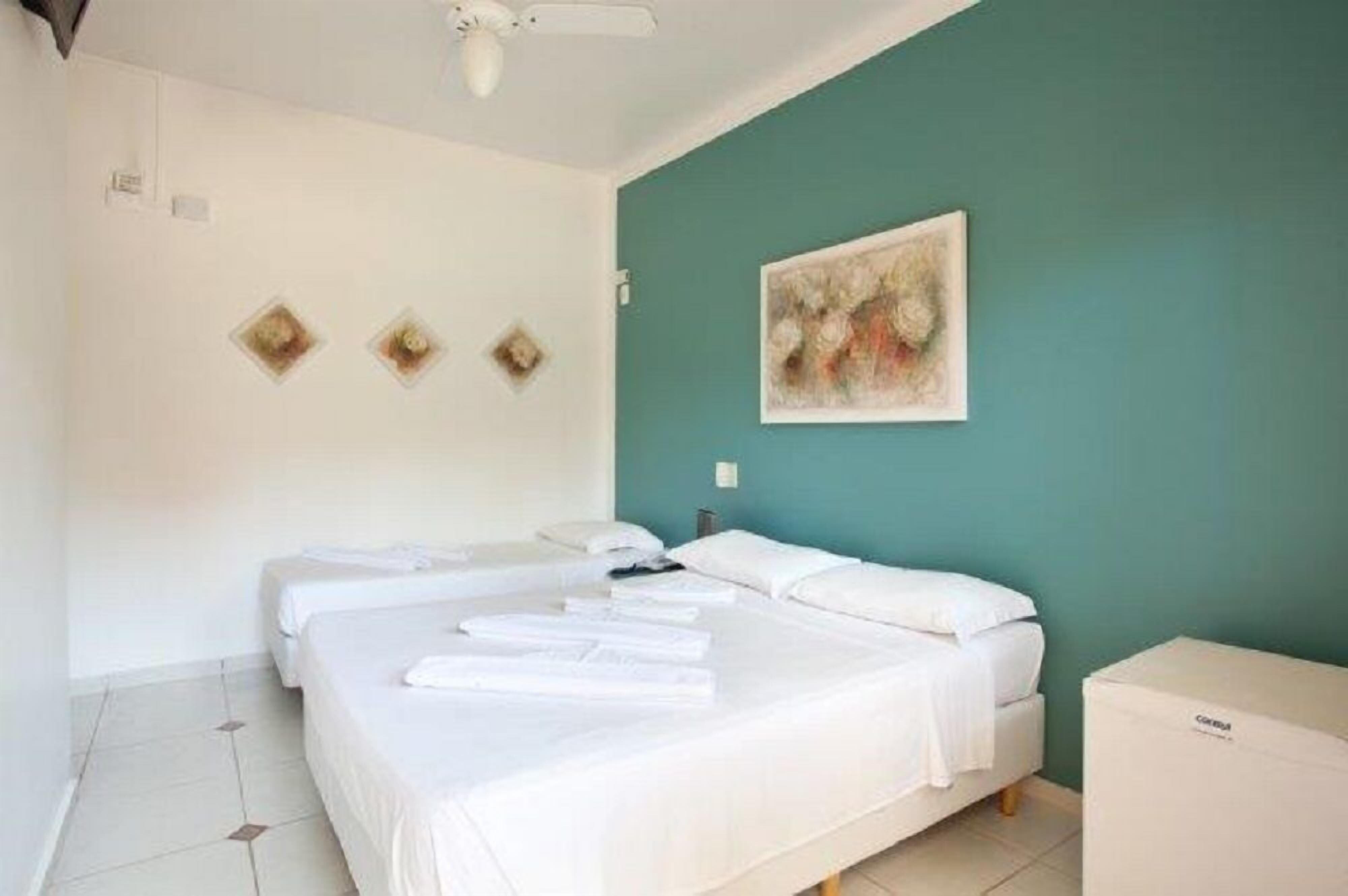A hotel room with two beds, a teal accent wall, and a painting.