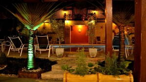 An outdoor seating area with chairs and planters, a pool, and a building with a red wall and starfish decorations. - Pousada Camburioca (São Sebastião)