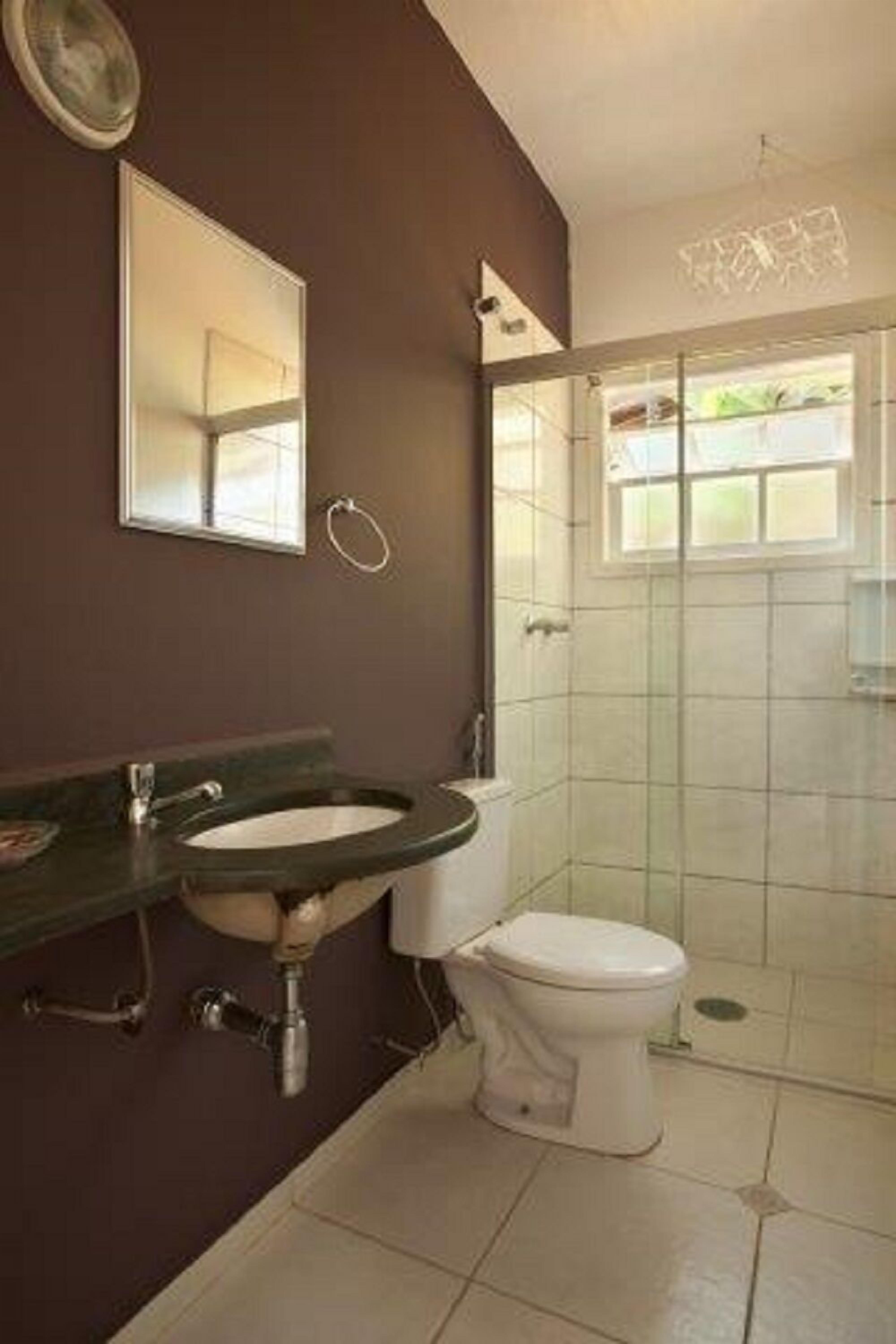Ein Badezimmer mit dunkelbrauner Wand, einem weißen Waschbecken, einer Toilette und einer Duschkabine aus Glas.