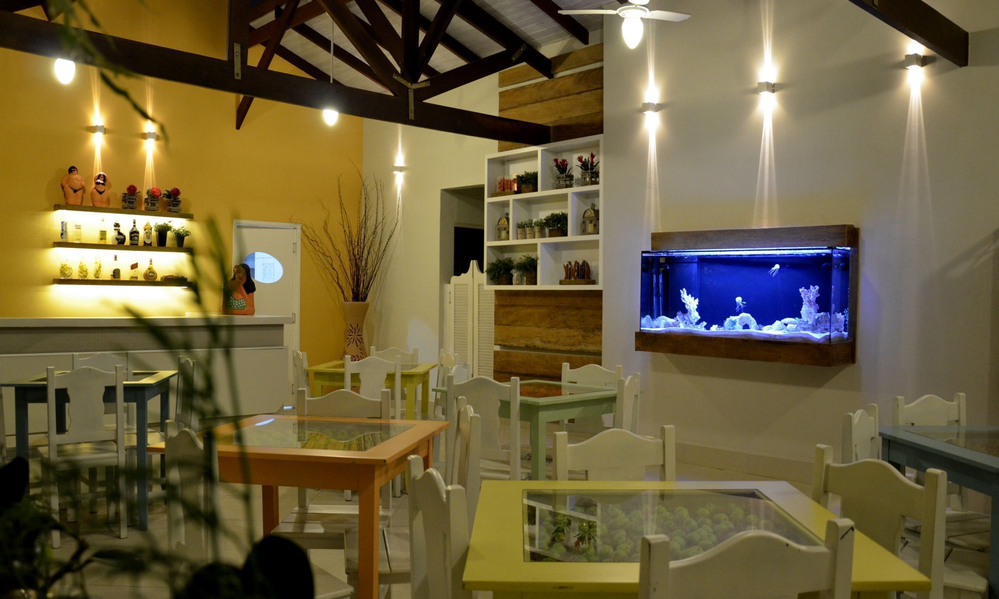 A restaurant with white chairs and tables, a wall-mounted aquarium, and shelves with various items.
