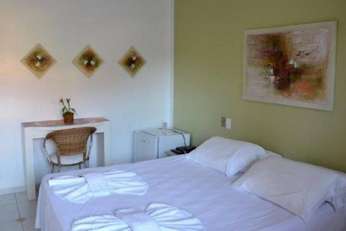 Um quarto com cama, escrivaninha, cadeira e uma pequena mesa.
