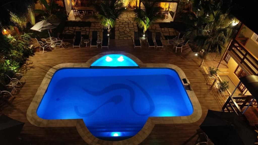 An outdoor swimming pool with a stone border, surrounded by lounge chairs and umbrellas, and palm trees.