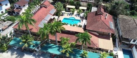 An aerial view of a residential area with a swimming pool surrounded by palm trees and a red-roofed building.