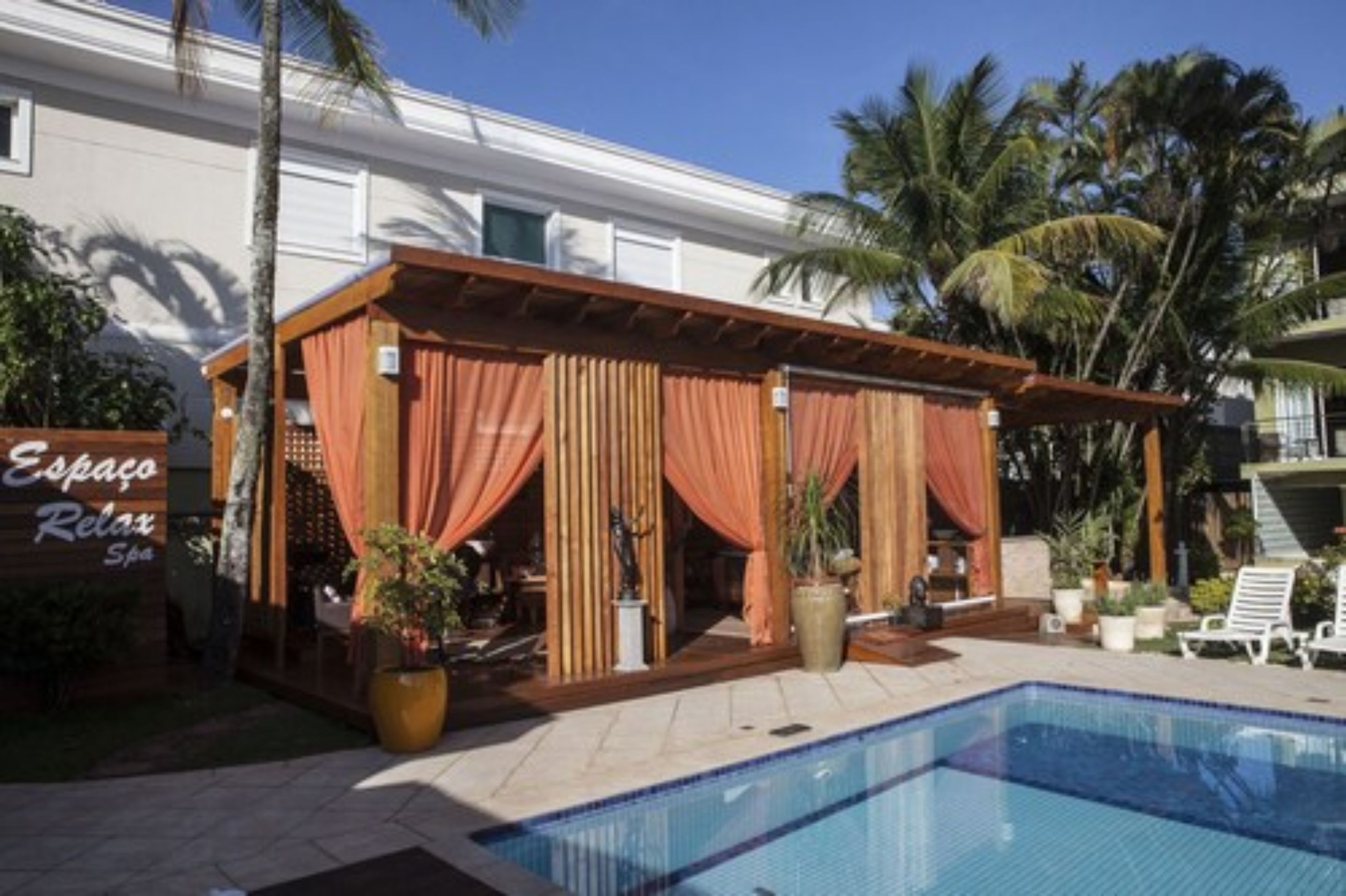 Un área junto a la piscina con una zona de estar techada, un letrero que dice "Espaço Relax Spa" y una piscina azul cristalina.