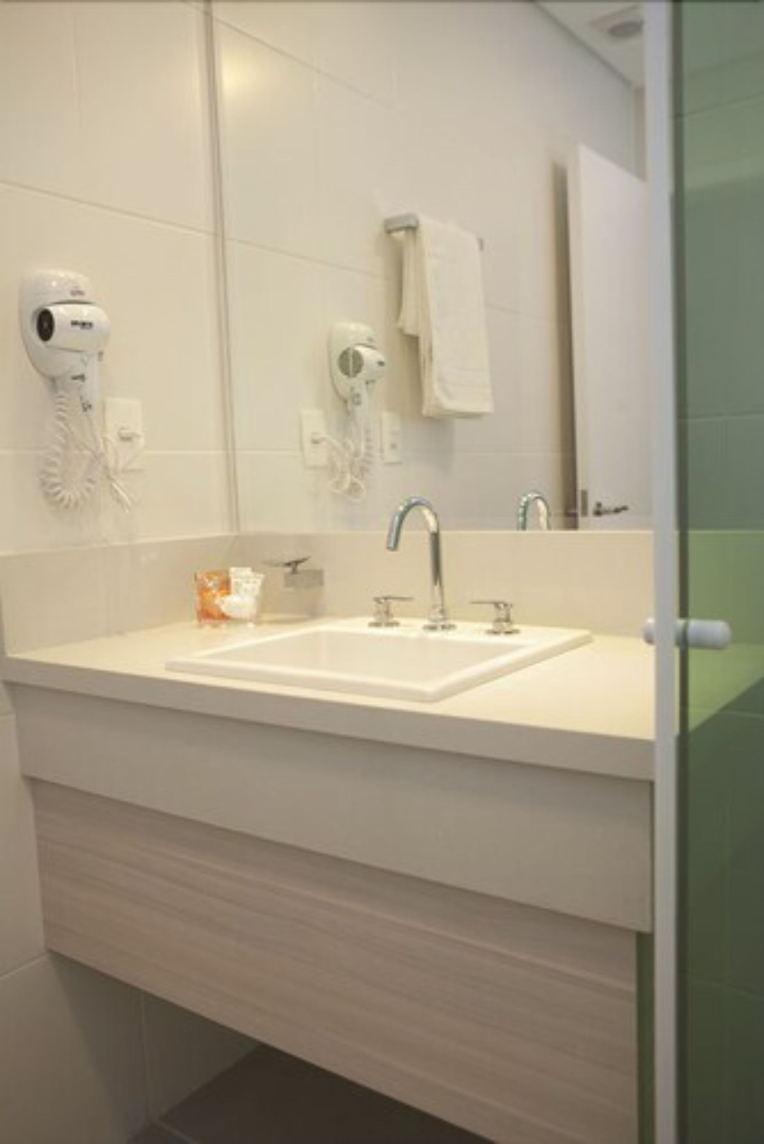 A bathroom with a white sink, two faucets, a mirror, and a hairdryer mounted on the wall.