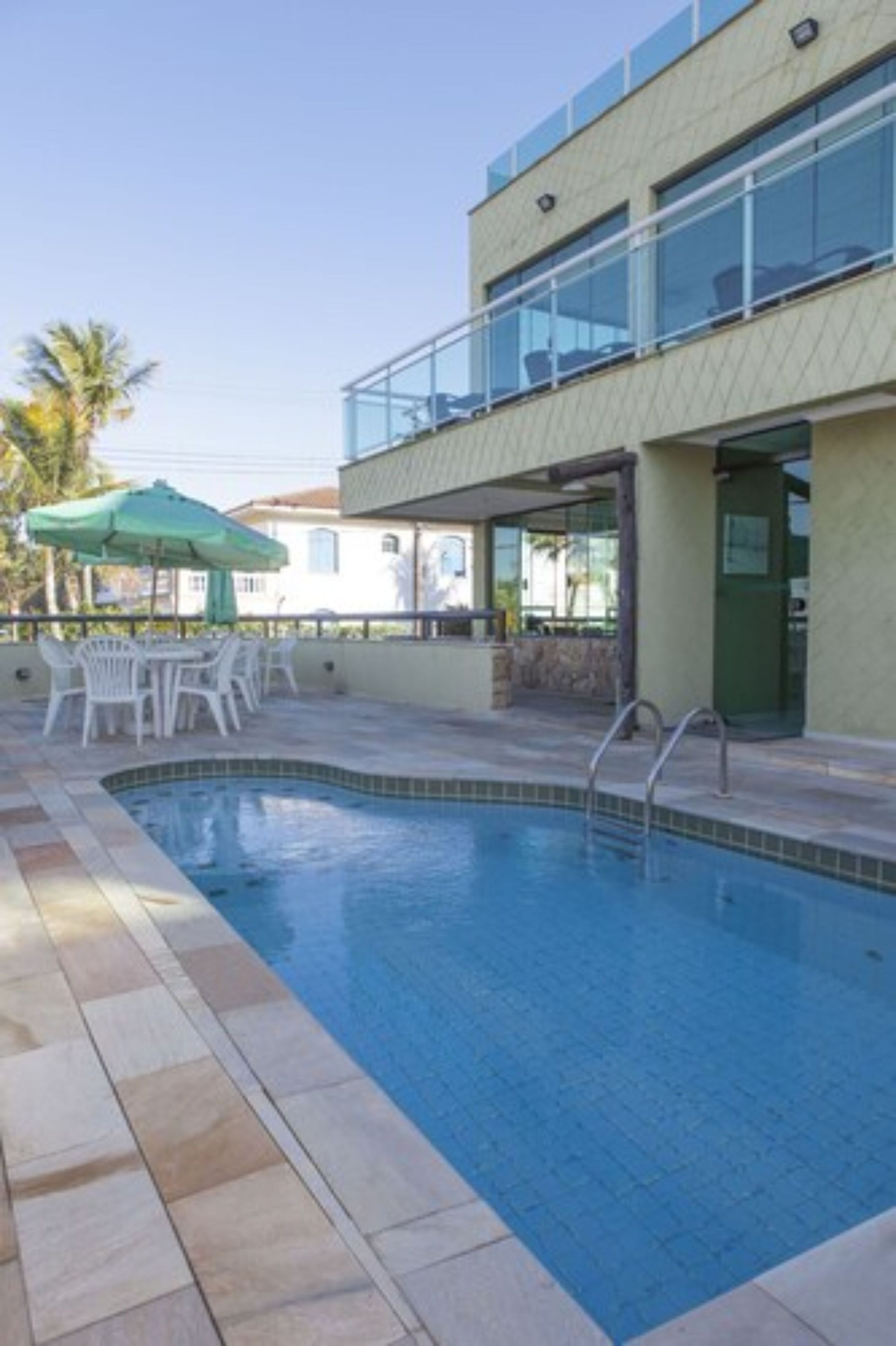 A swimming pool with a tiled deck, outdoor seating, and a building with large windows in the background.
