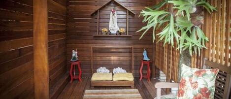 A wooden room with a bench, a small table, and a wall-mounted shelf with a statue.