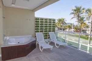 Un balcón con un jacuzzi, dos sillones blancos y una pared verde.