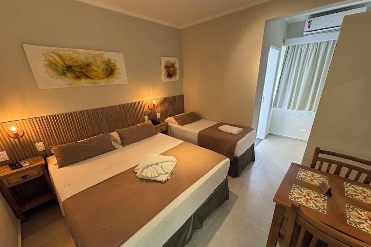 Une chambre d’hôtel avec deux lits, une tête de lit en bois, une table à manger et des œuvres d’art accrochées au mur.