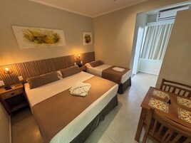 Habitación de hotel con dos camas, cabecero de madera, una mesa de comedor y obras de arte en la pared.