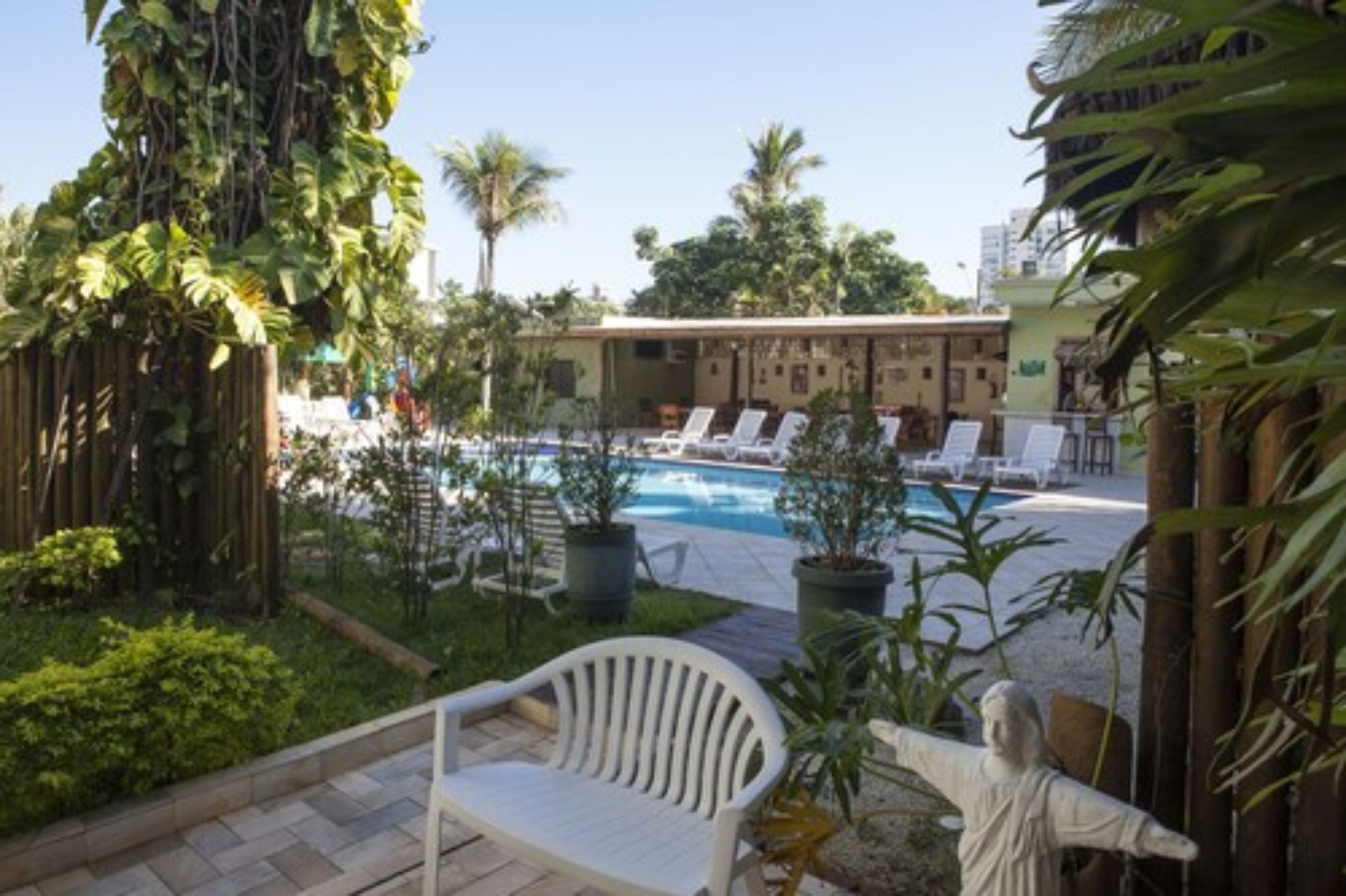 A pool area with lounge chairs, a statue, and tropical plants.
