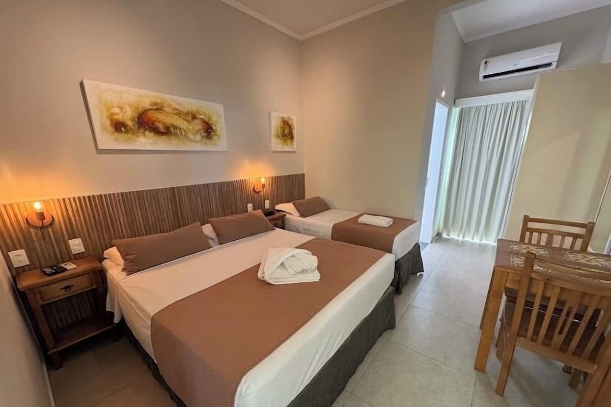 Une chambre d’hôtel avec deux lits, une tête de lit en bois, une table à manger avec des chaises et des œuvres d’art accrochées au mur.