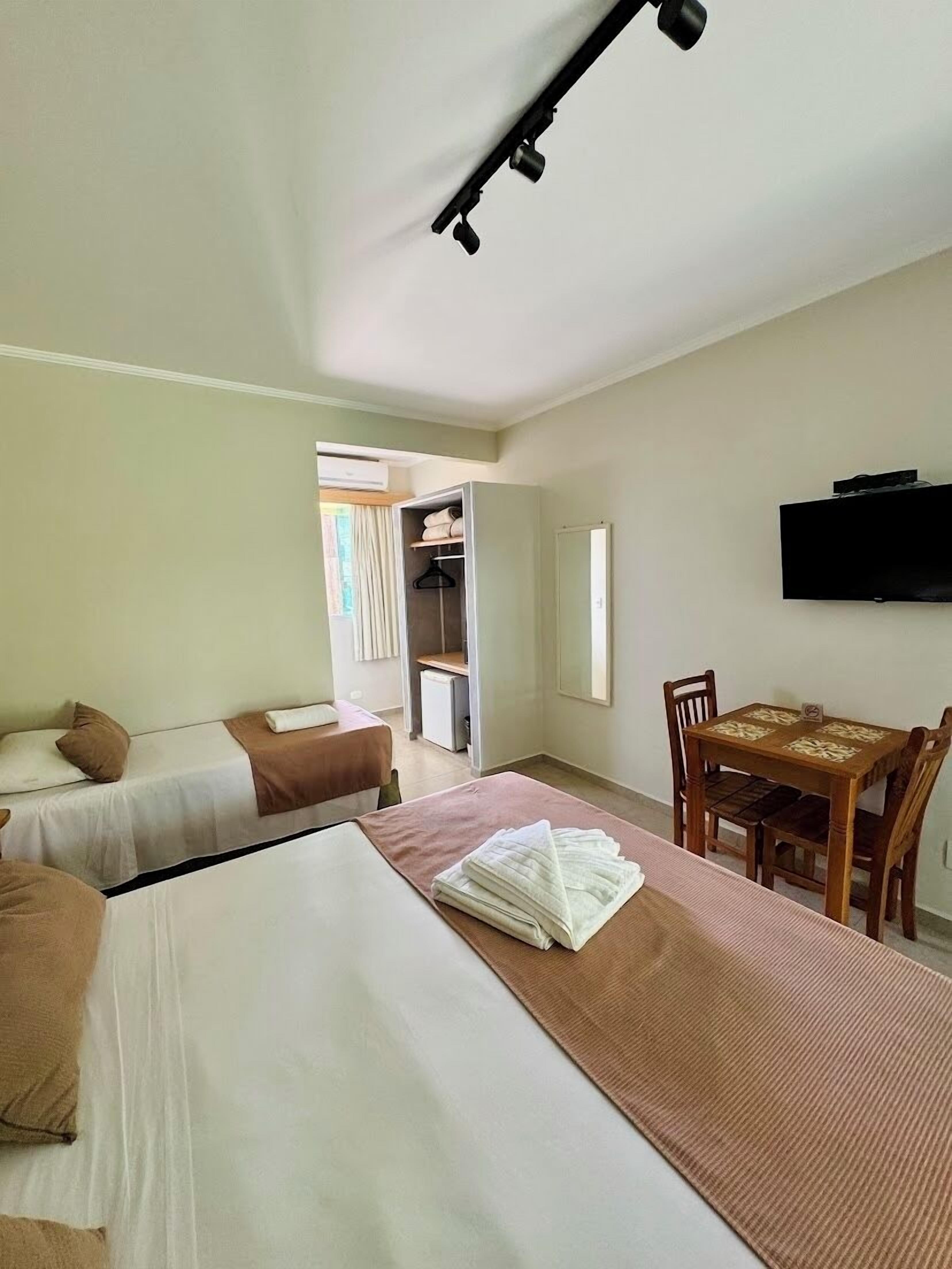 A hotel room with two beds, a dining table with chairs, a TV mounted on the wall, and a closet with a mirror.