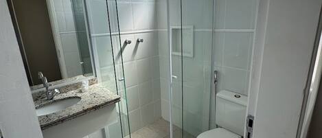 Un baño moderno con ducha de vidrio, inodoro y lavamanos con encimera de mármol.