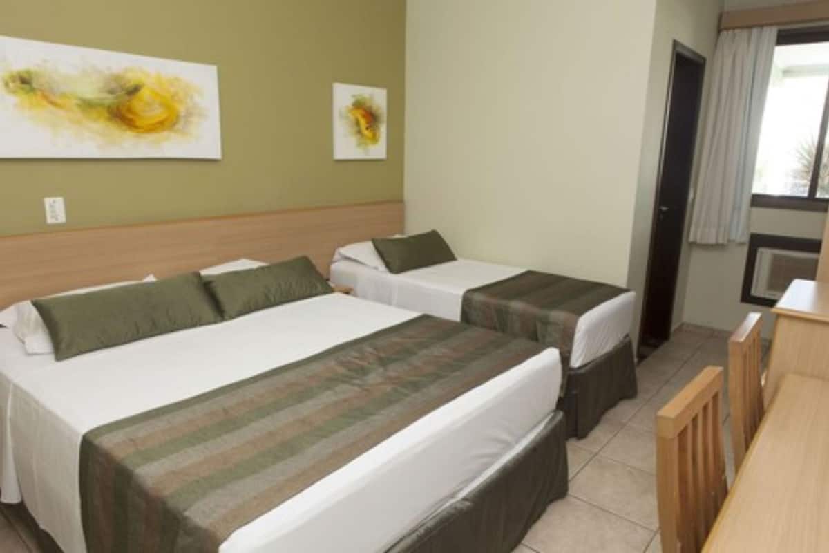 Une chambre d’hôtel avec deux lits, une tête de lit en bois, un bureau et une fenêtre avec des rideaux.