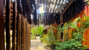 A narrow pathway leading to a wooden structure with a thatched roof, surrounded by lush greenery and a gravel path with circular mats. - Pousada Papaya (Ubatuba)
