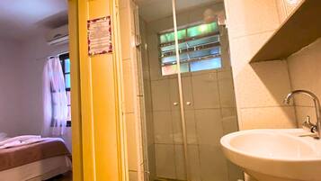 Une salle de bain avec une porte de douche en verre, un lavabo et un lit dans la pièce adjacente.