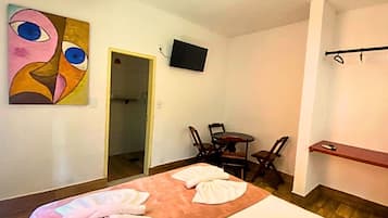 Habitación de hotel con cama, un cuadro en la pared, televisor y una pequeña mesa con sillas.