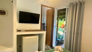 A hotel room with a bed, a television on a stand, a small refrigerator, and a view of the outside through a door. - Pousada Papaya (Ubatuba)