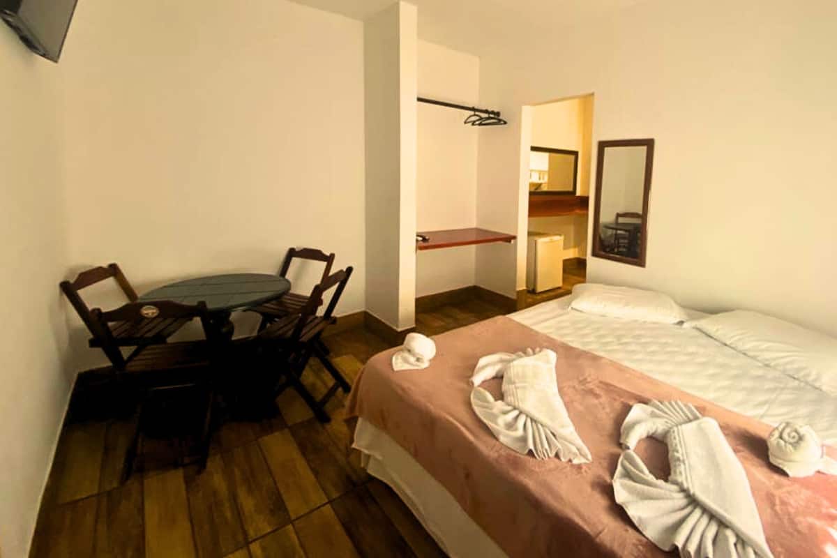 Ein Hotelzimmer mit Bett, Schreibtisch, Stuhl, einer kleinen Küchenzeile und einem Spiegel.