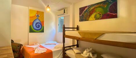 Una habitación con literas, una mesita con una toalla y dos cuadros en la pared.