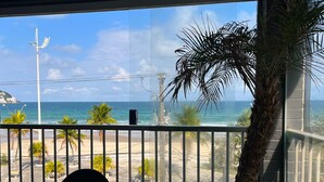 Une vue depuis un balcon donnant sur une plage bordée de palmiers, sous un ciel dégagé.