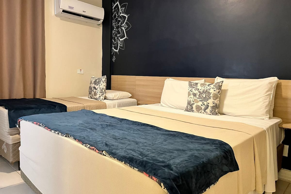 A hotel room with a bed, a bedside table, a wall-mounted air conditioner, and a decorative wall piece.