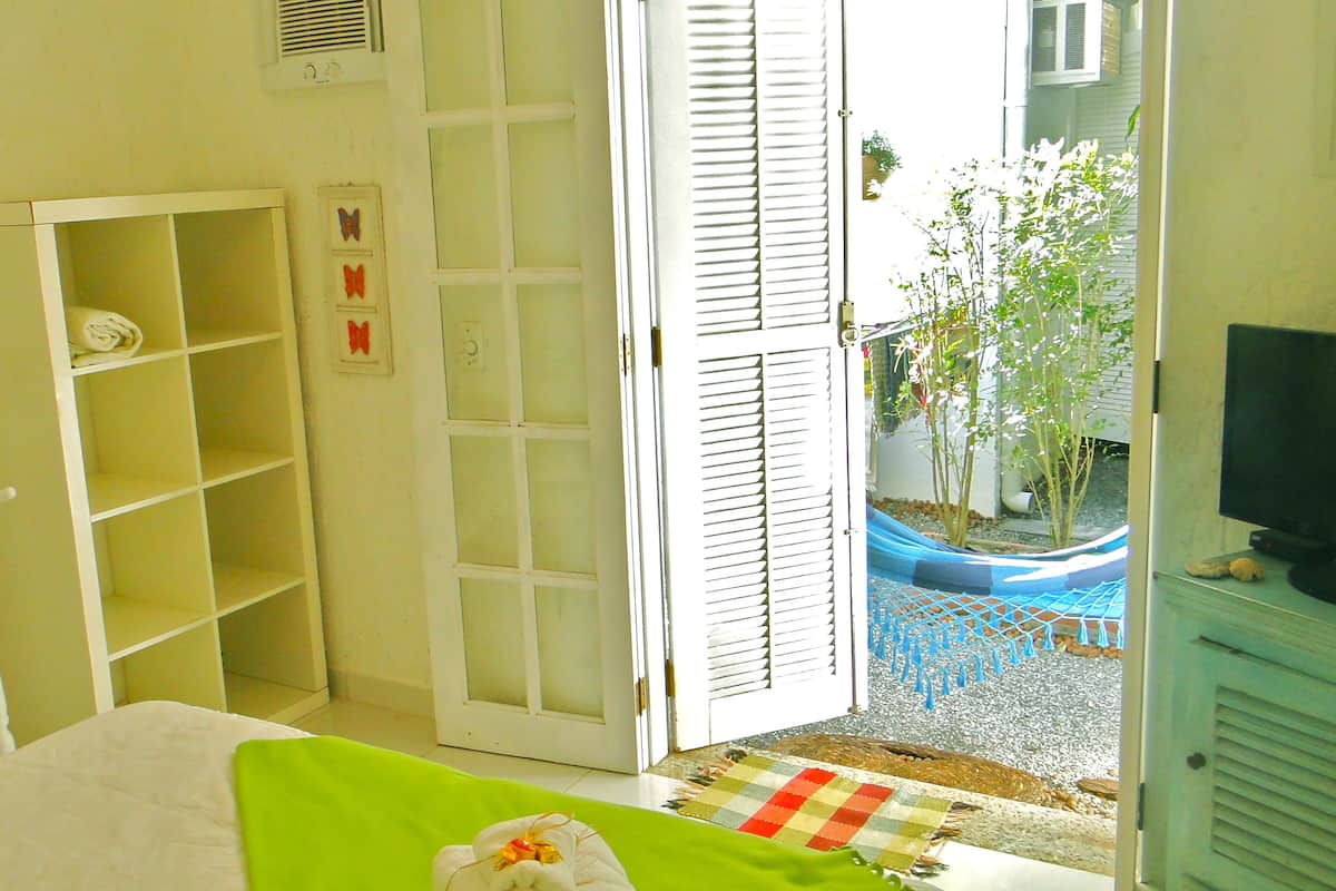 A room with a bed, a wardrobe, and a door leading to a balcony with a blue net and plants.