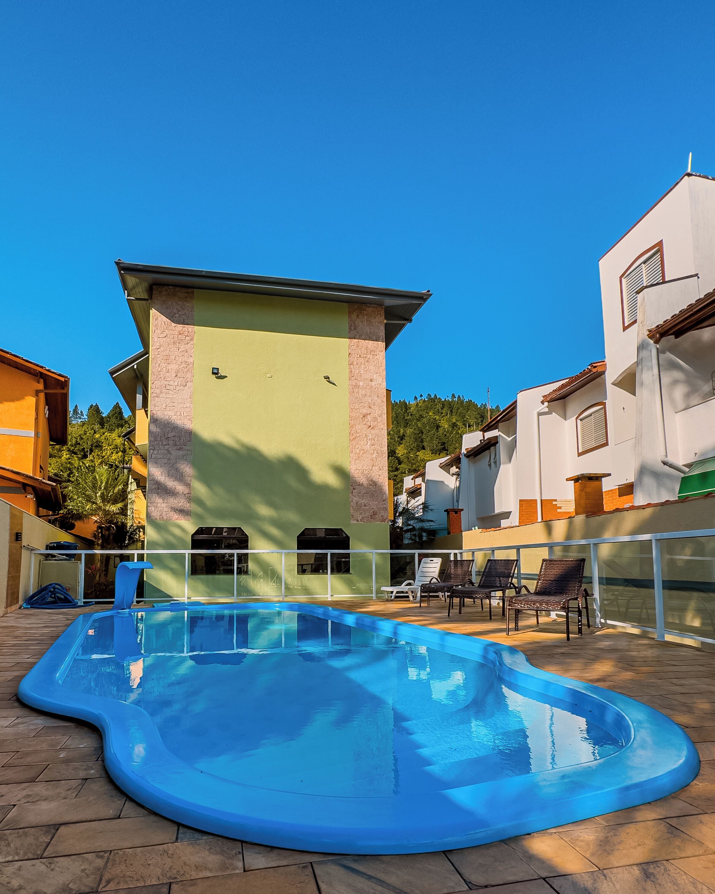 A swimming pool with a curved edge, surrounded by lounge chairs and a building with a light green facade and a stone pillar.