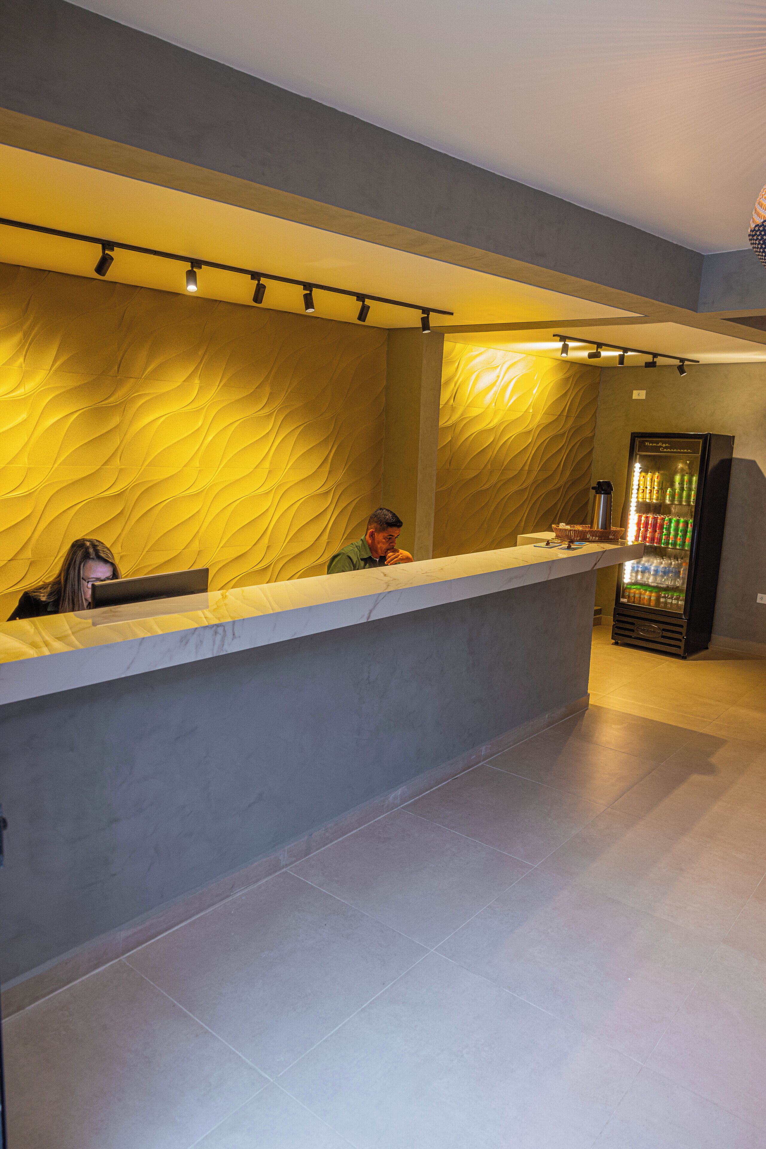 Zona de recepción con mostrador, pared con diseño texturizado y dispensador de bebidas.