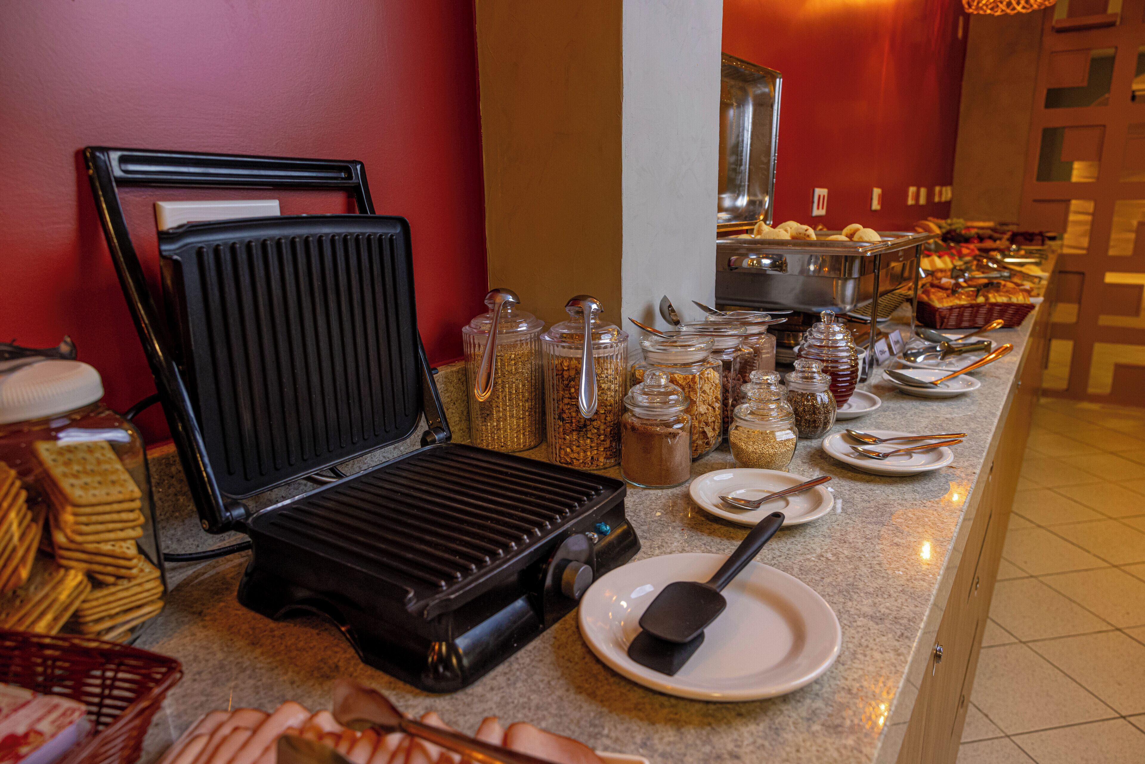 Montaje de bufé con una parrilla, distintos recipientes de comida y cubiertos.