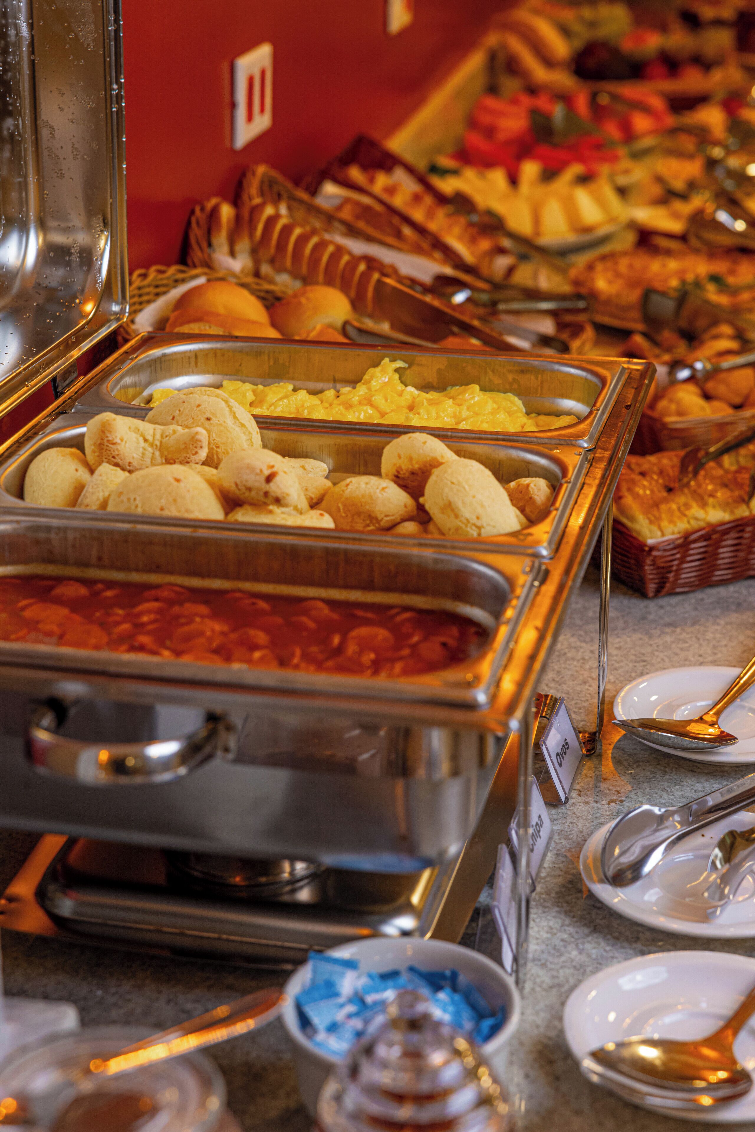 Un bufé con diversos alimentos en recipientes metálicos, incluyendo pan, bollería y otros platos.
