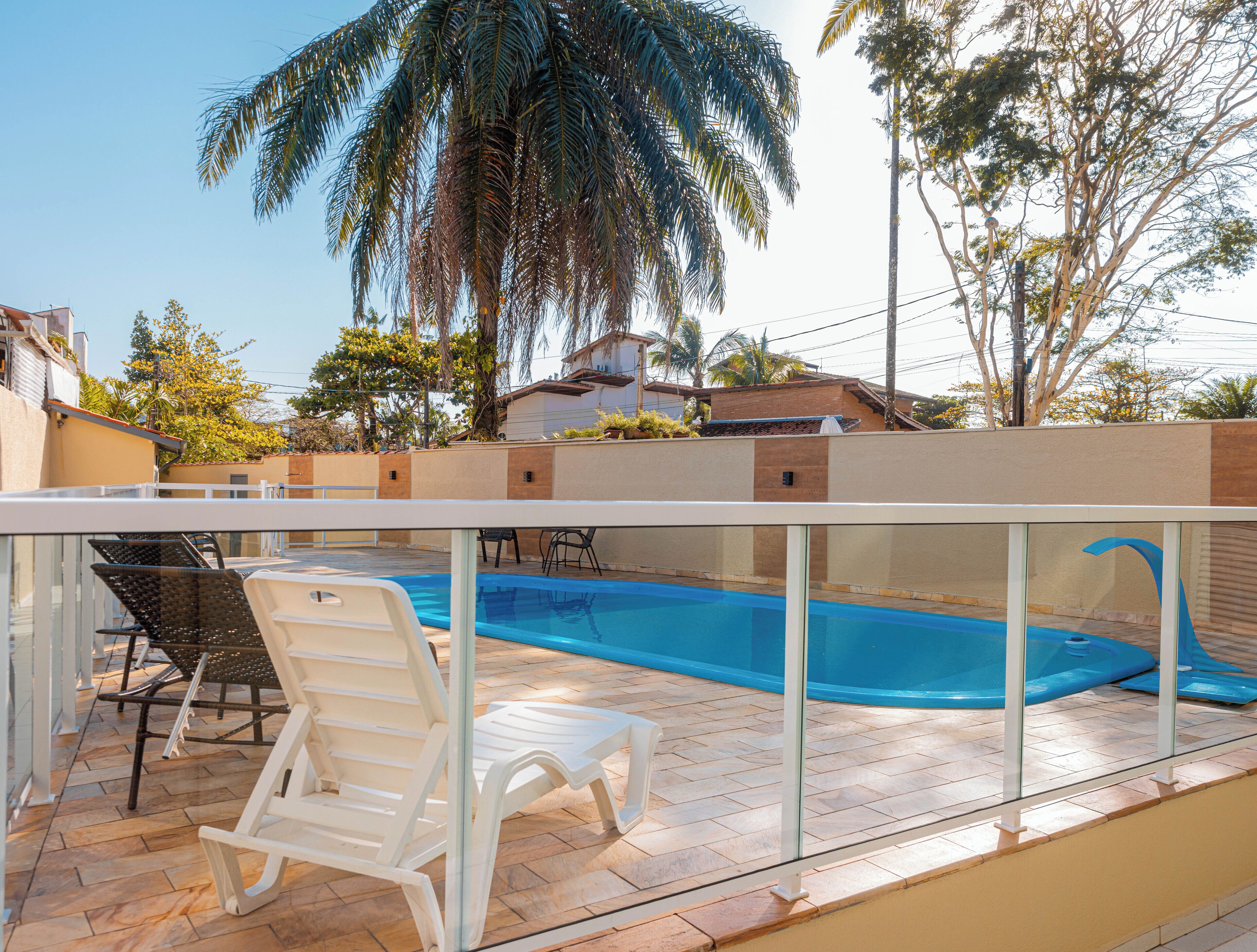 A swimming pool with clear blue water, surrounded by a glass railing. There are white lounge chairs and a table near the pool.