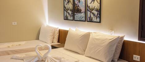 A hotel room with two beds, white linens, heart-shaped towels, and three framed pictures on the wall.