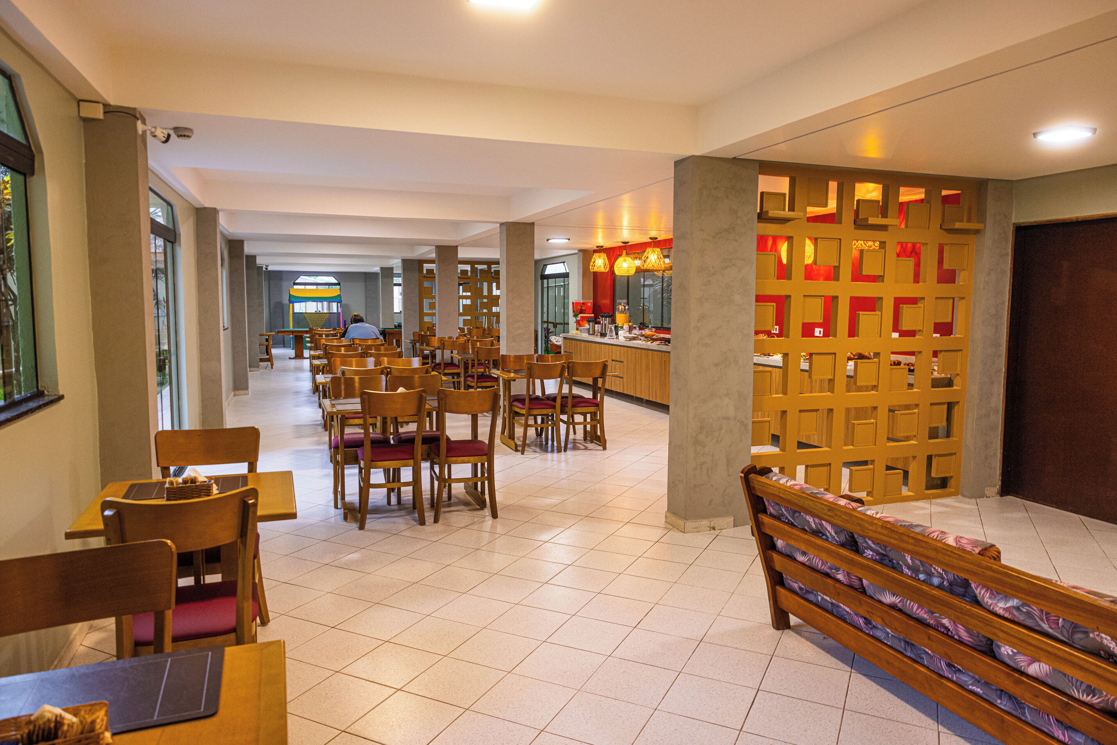 A hotel lobby with wooden chairs and tables, a reception desk, and a decorative wall with geometric patterns.