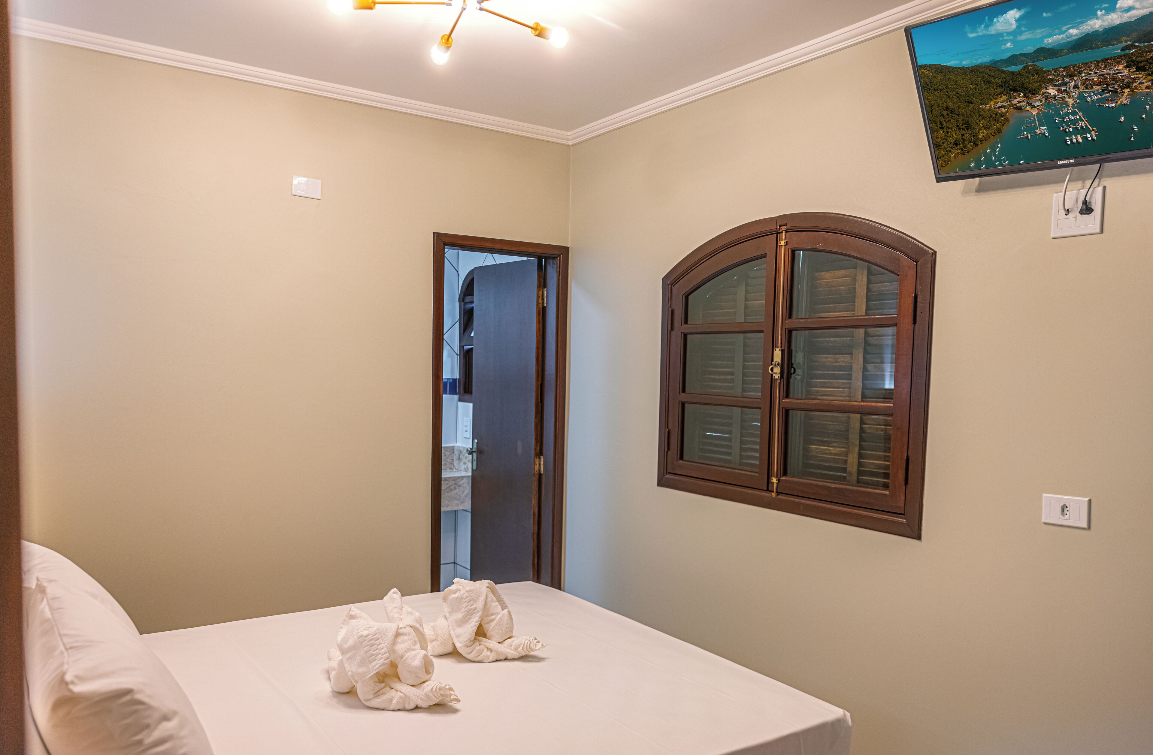 A bedroom with a bed, a window, and a TV on the wall.