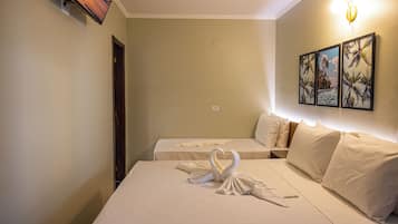 A hotel room with two beds, a wall-mounted TV, and a painting of palm trees.
