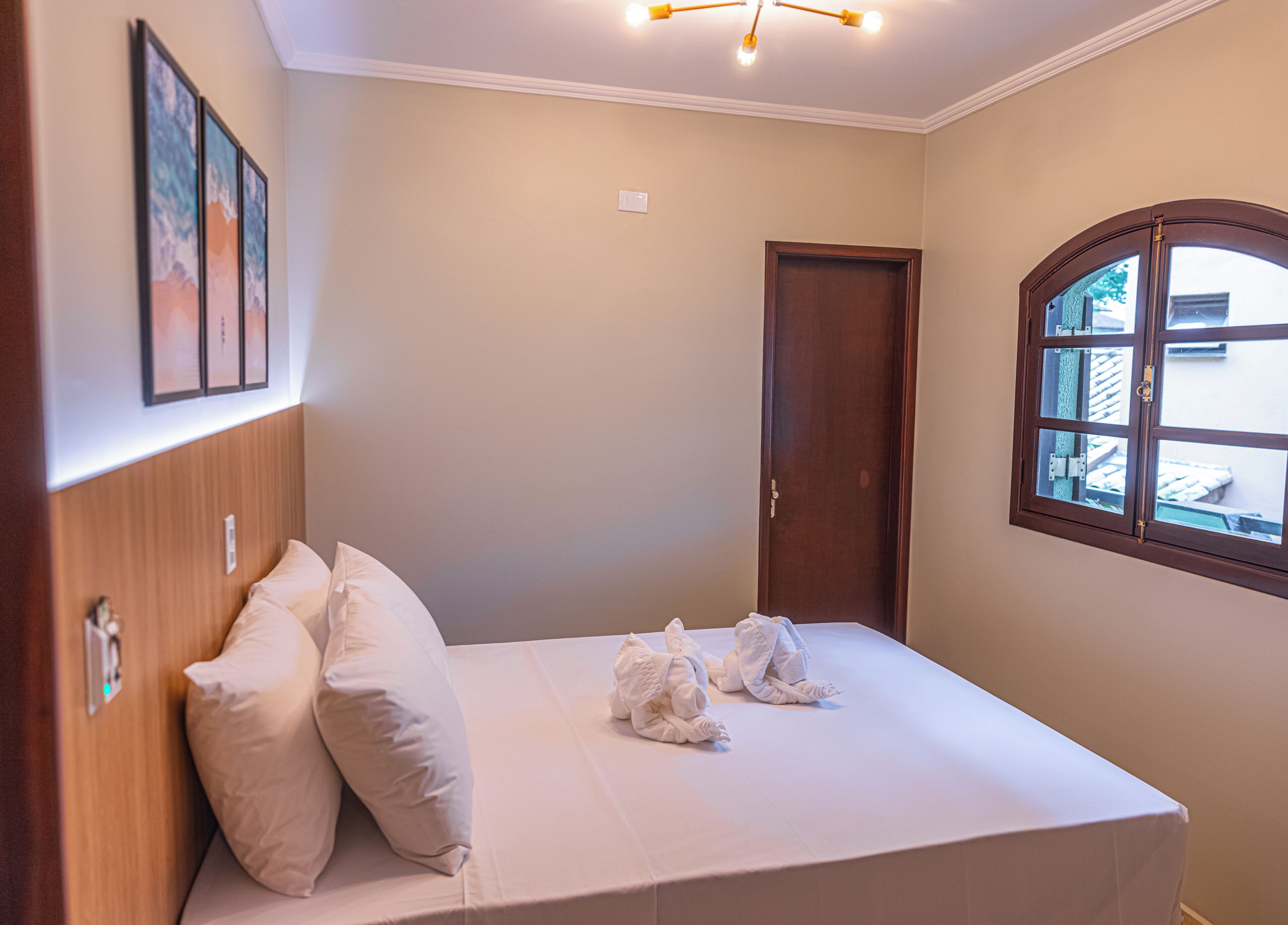 A neatly made bed with pillows, a wooden headboard, a window with a view of the outside, and a door.