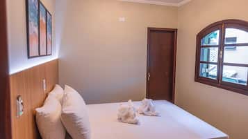 A neatly made bed with pillows, a wooden headboard, a window with a view of the outside, and a door.
