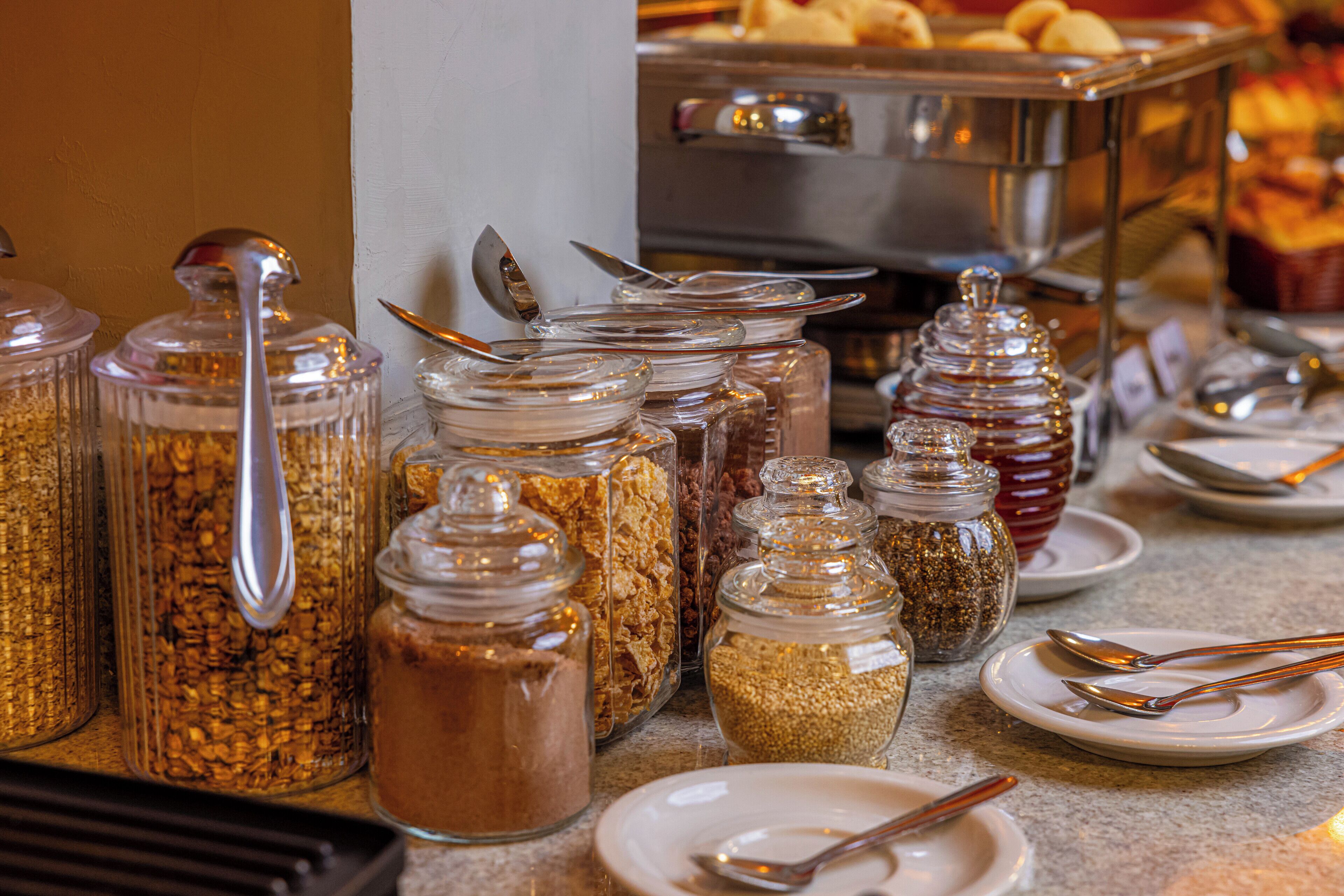 A buffet setup with various food items in glass containers, accompanied by serving utensils and plates.