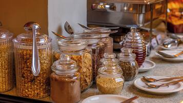 Montaje de buffet con diversos alimentos en recipientes de vidrio, acompañado de utensilios y platos.
