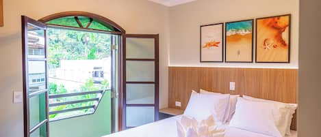 Un cuarto de hotel con una cama, un balcón que ofrece vistas a la vegetación y tres cuadros en la pared.