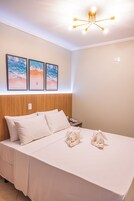 A neatly made bed with white linens and two decorative pillows, a wooden headboard, and a wall-mounted light fixture.