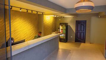 Un área de recepción con mostrador de mármol, pared con textura, refrigerador para bebidas y puerta de diseño único.
