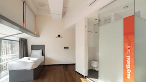 A modern hotel room with a bed, a shower area, and a glass partition.