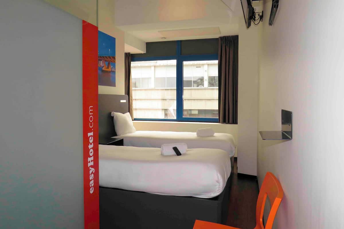 A hotel room with two beds, a window with curtains, a chair, and a wall-mounted TV.
