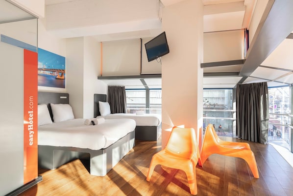 A hotel room with a bed, a desk, a chair, a TV, and a view of the city.
