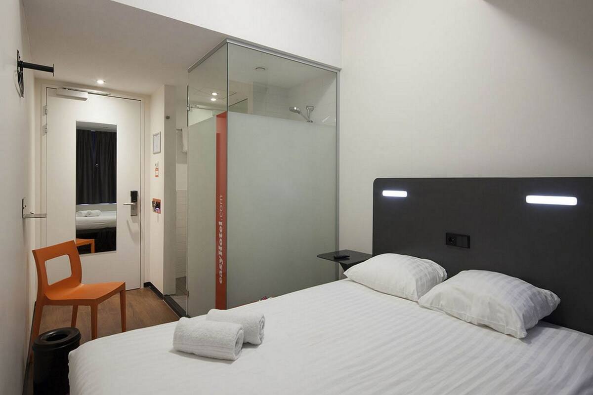 A modern hotel room with a bed, a chair, a small table, and a glass partition.