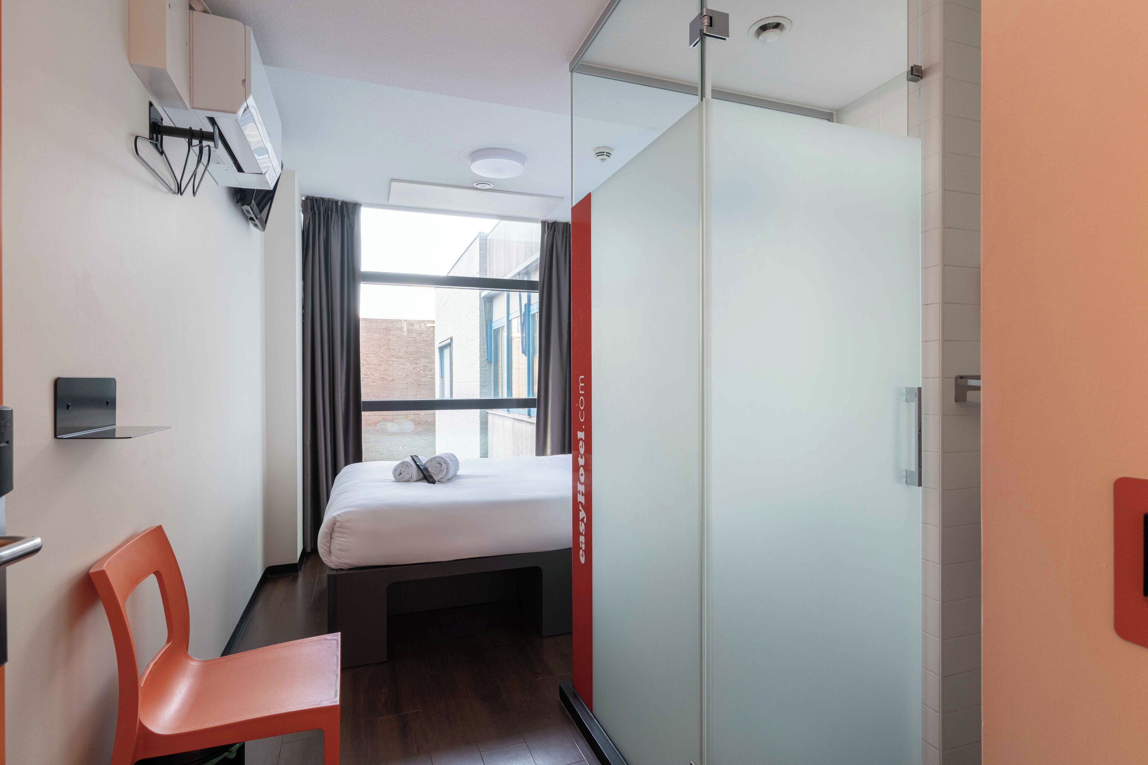 Une chambre d’hôtel comprenant un lit, une chaise, un bureau, une fenêtre avec des rideaux et une porte coulissante.