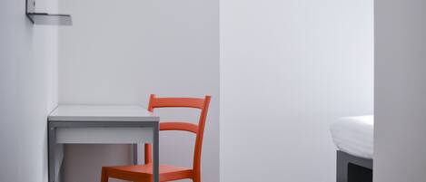 Una habitación pequeña y sencilla con escritorio, silla y cama.